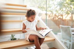 Hispanic Girl Sitting On Staircase In Modern Home Reading Book